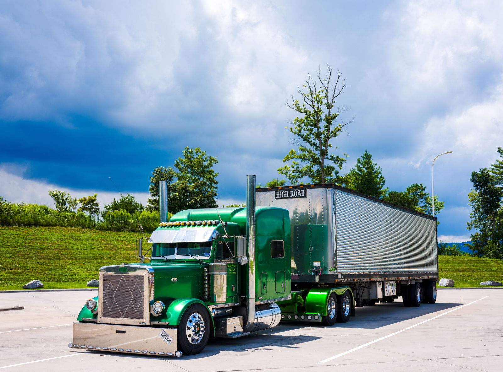Green American semi-truck with trailer parked beside a grassy slope