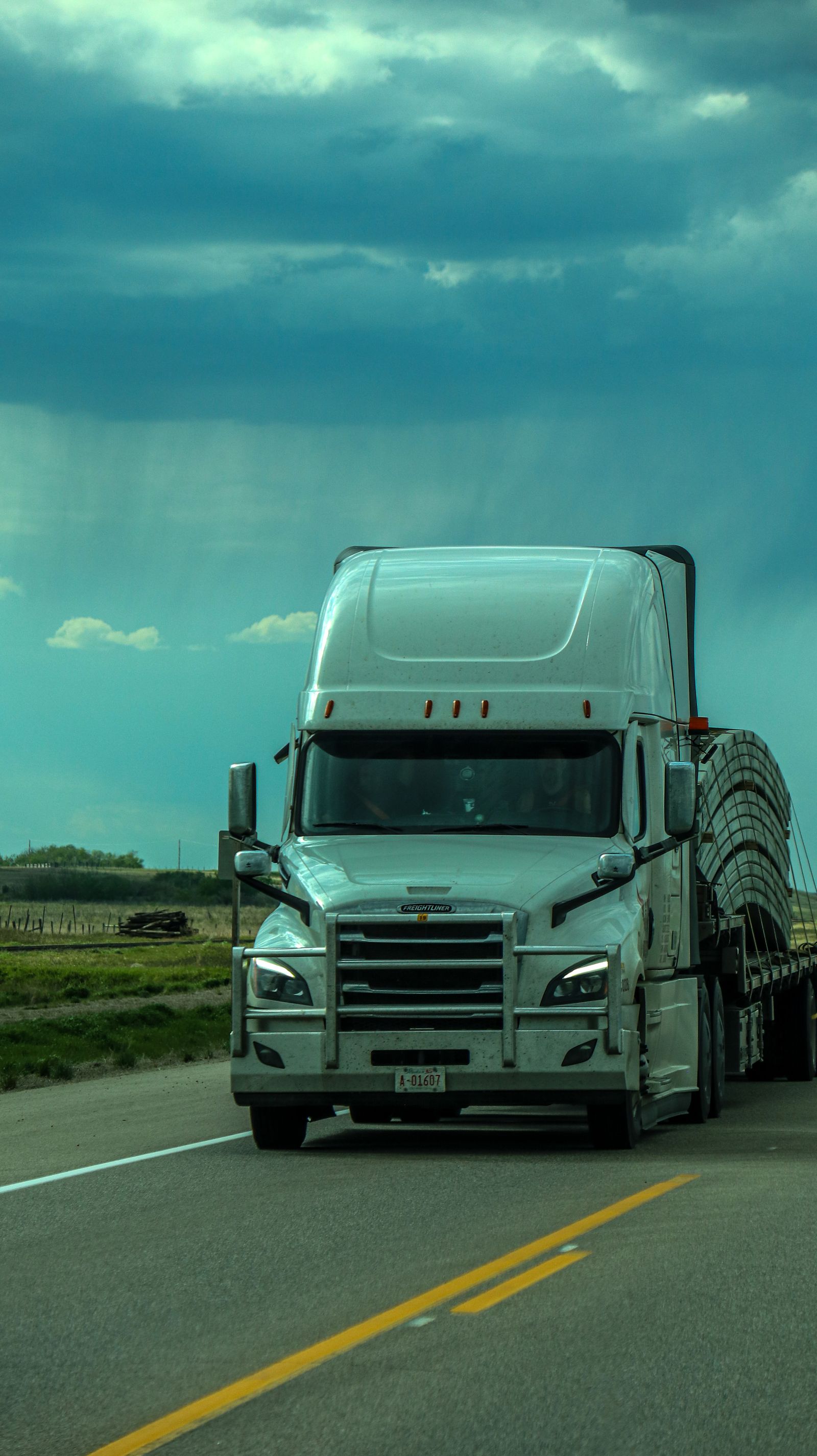 White American semi-truck traveling on a rural highway under a cloudy sky